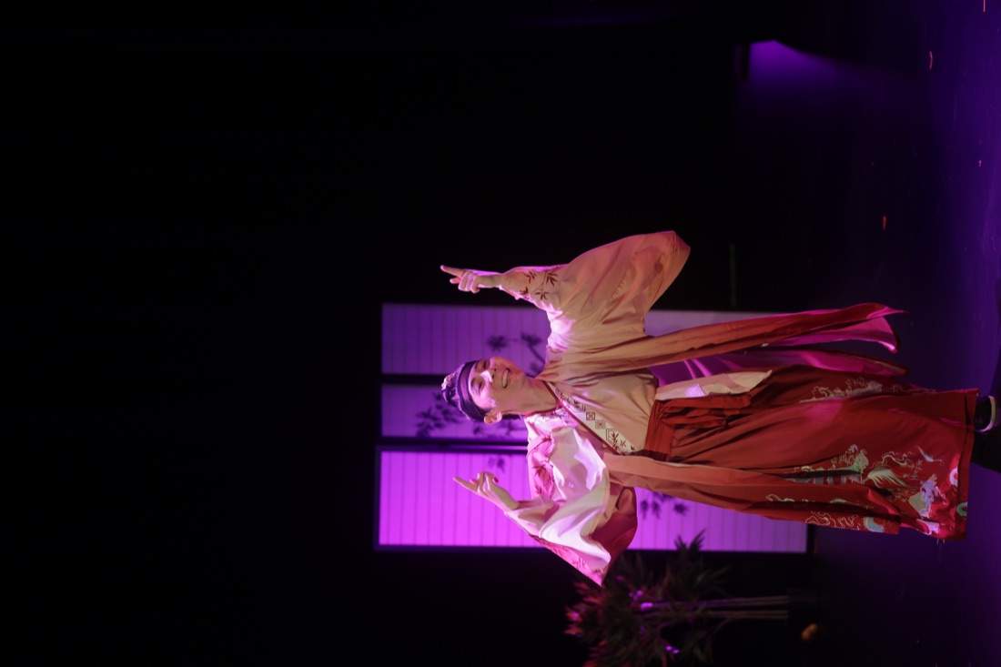 Hua performs alone in a pink robe under magenta stage light.