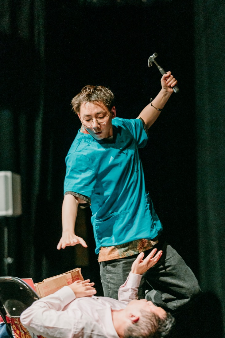 Hua raises a prop hammer during an exaggerated stage operation.