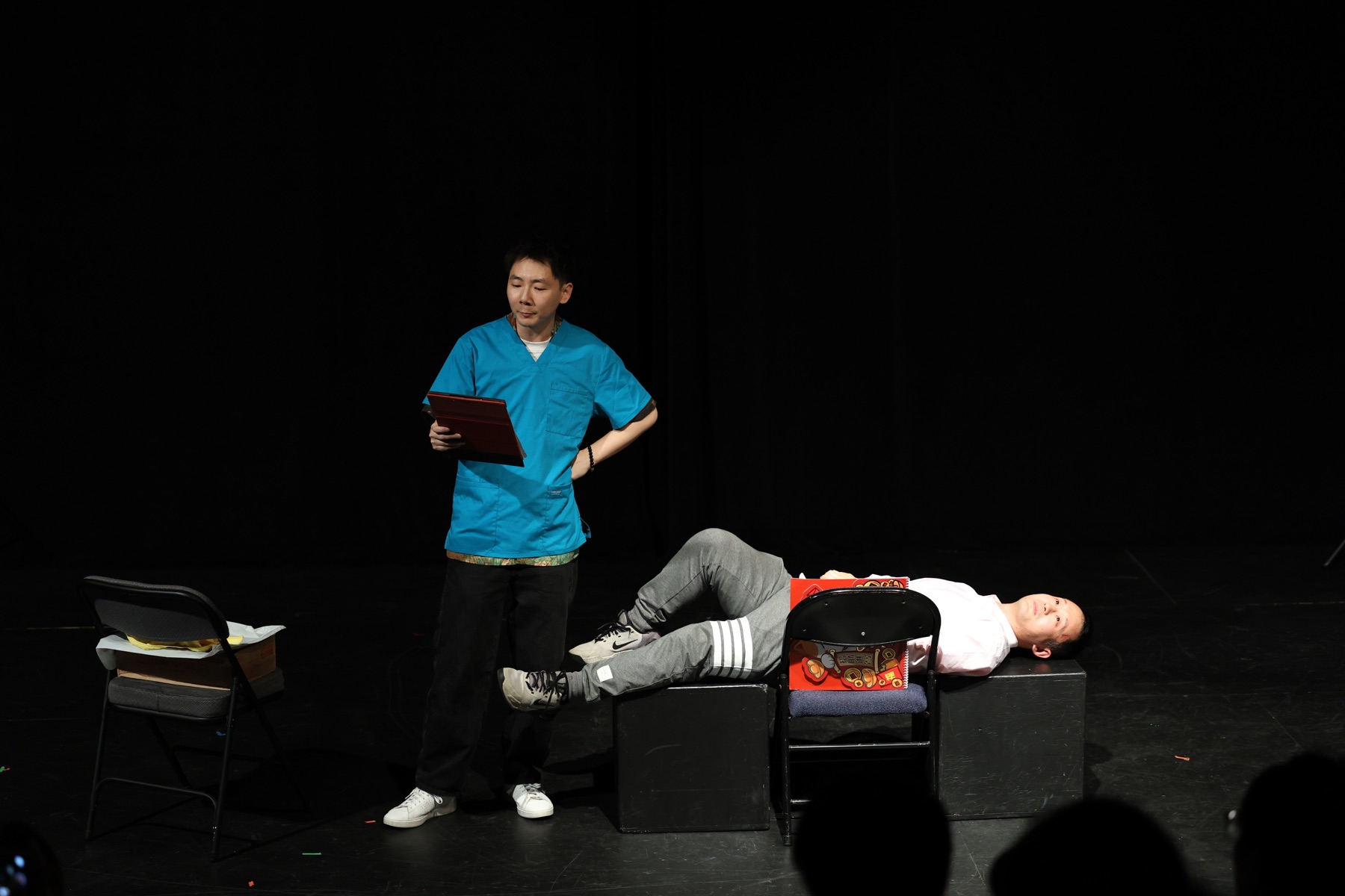 Hua performs as a surgeon beside a patient stretched across stage furniture.