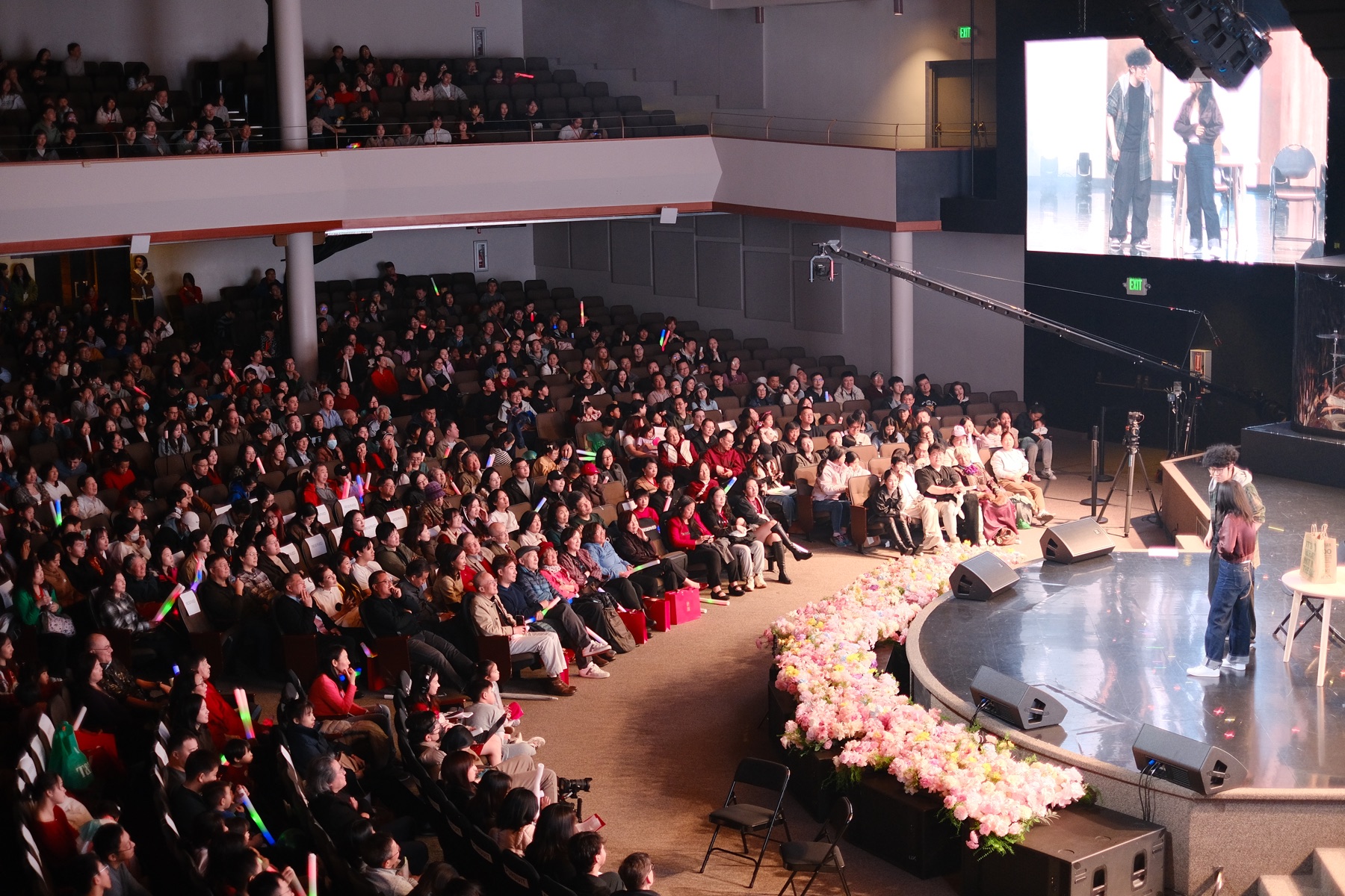 A large theatre audience watches Crazy Delivery from beside the stage.