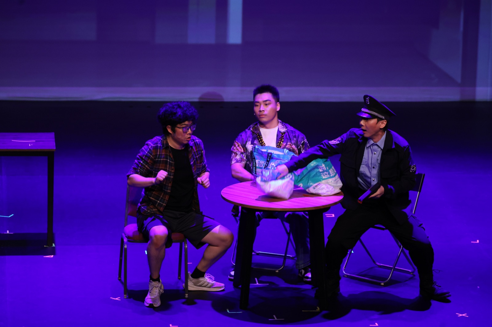 Four performers play a tense delivery scene under saturated purple stage light.