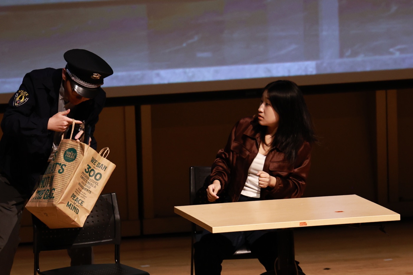Two performers act in a warm-lit university-stage production of Crazy Delivery.